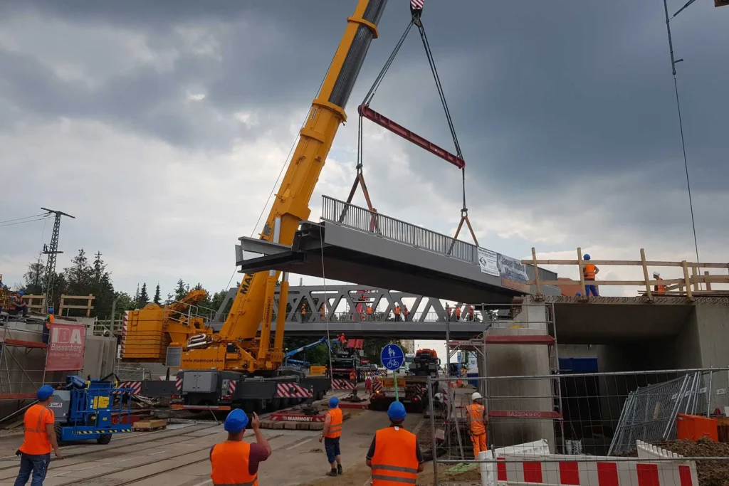 SIBAU Genthin GmbH & Co KG - Bauen auf Erfahrung - Referenzen Brückenbau - Baustelle Trogbrücke Hallew - Kran hebt Brückenbauteil - mehrere Bauarbeiter beteiligt